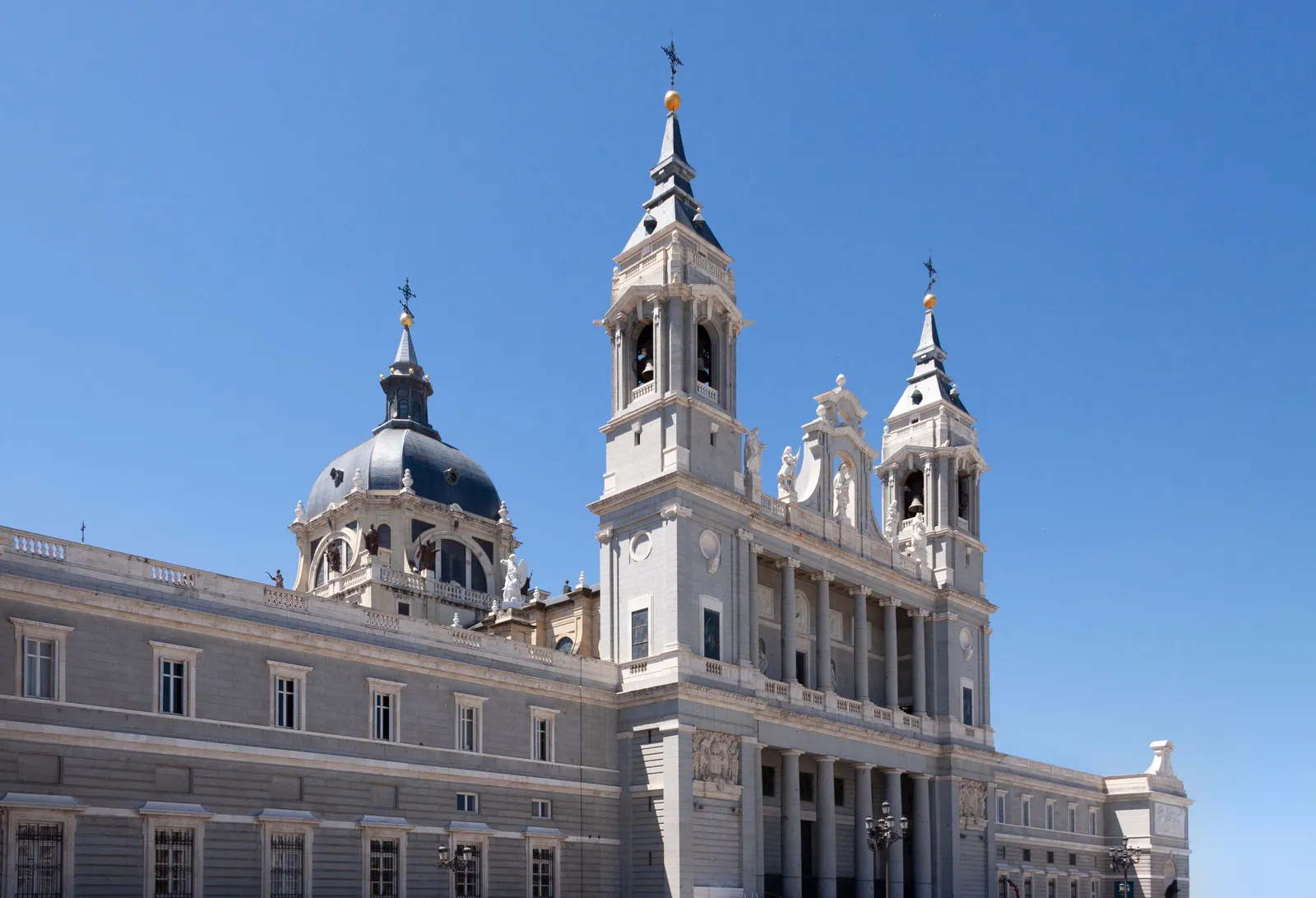 The pale stone facade and dome of the Almudena Cathedral beside the Royal Palace in Madrid under a clear sky, Spain