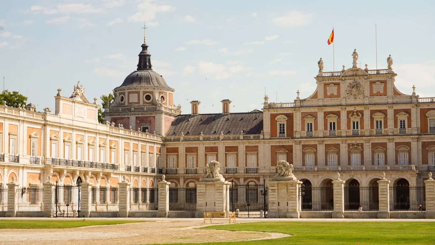 The symmetrical facade and formal front lawn of a grand Spanish royal palace under a clear sky