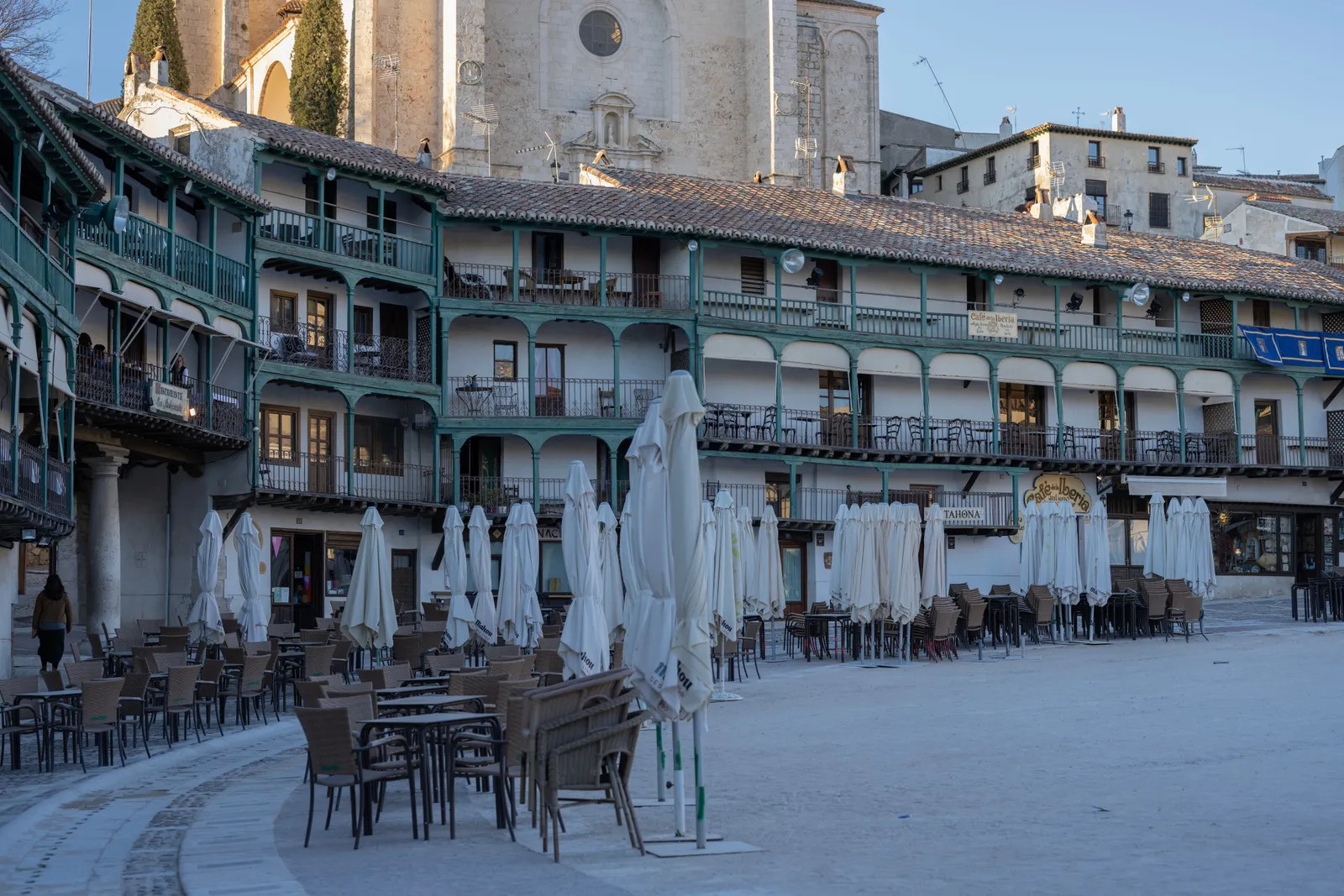 The circular Plaza Mayor of Chinchon with tiered wooden balconies, cafe tables and the church tower behind, Spain