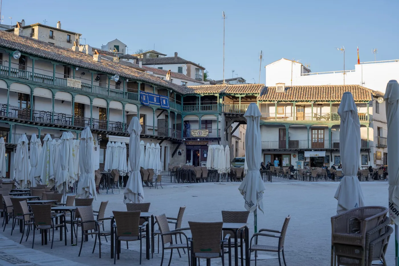 The tiered wooden balconies of Chinchon's Plaza Mayor with empty cafe tables as evening falls, Spain