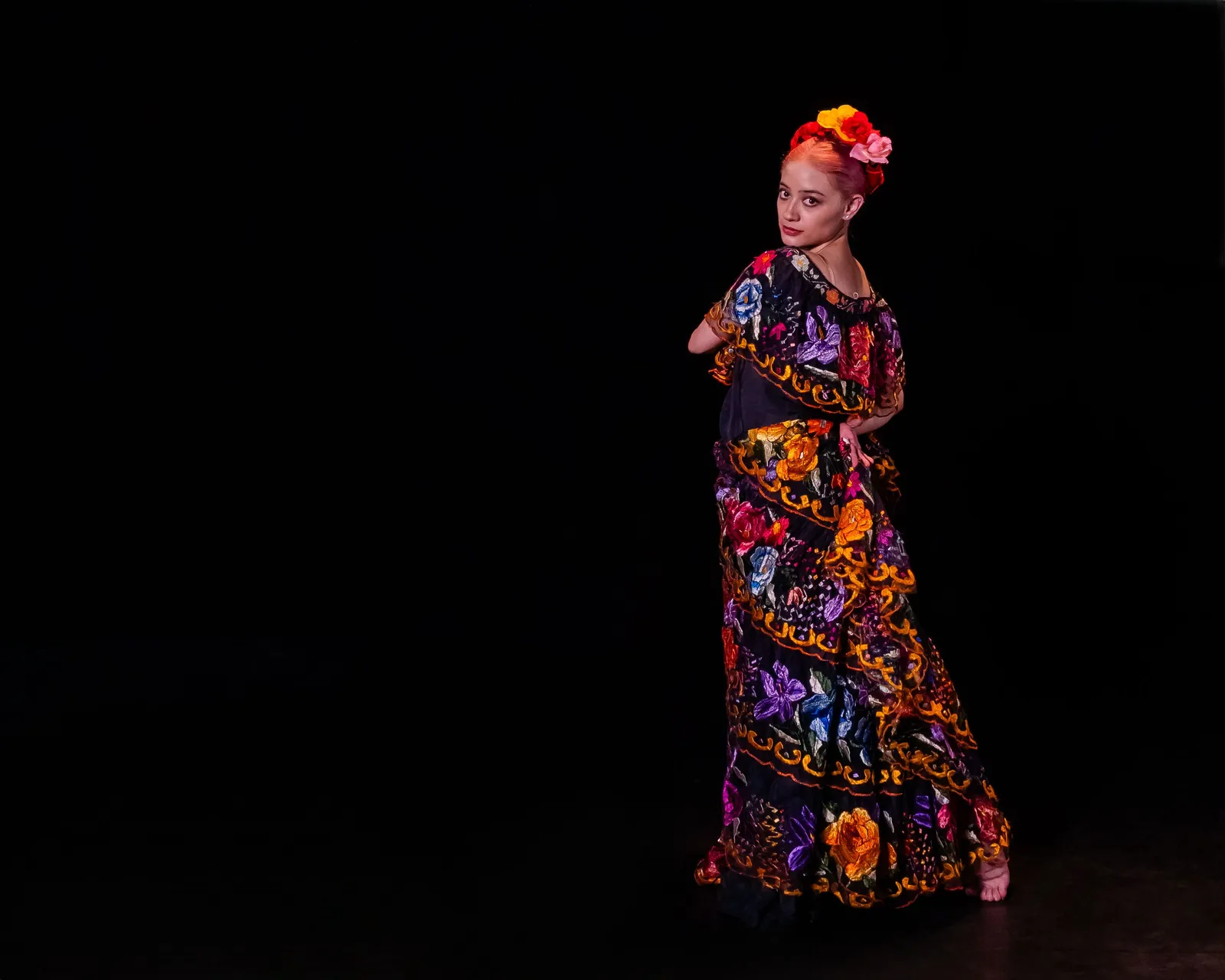 A flamenco dancer in a patterned dress performing against a dark background, Spain