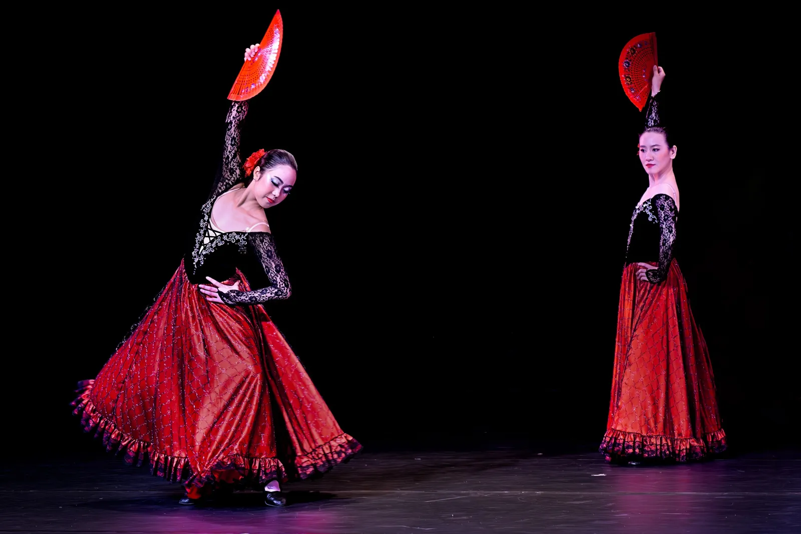 Two flamenco dancers with red fans raised on a stage, Spain