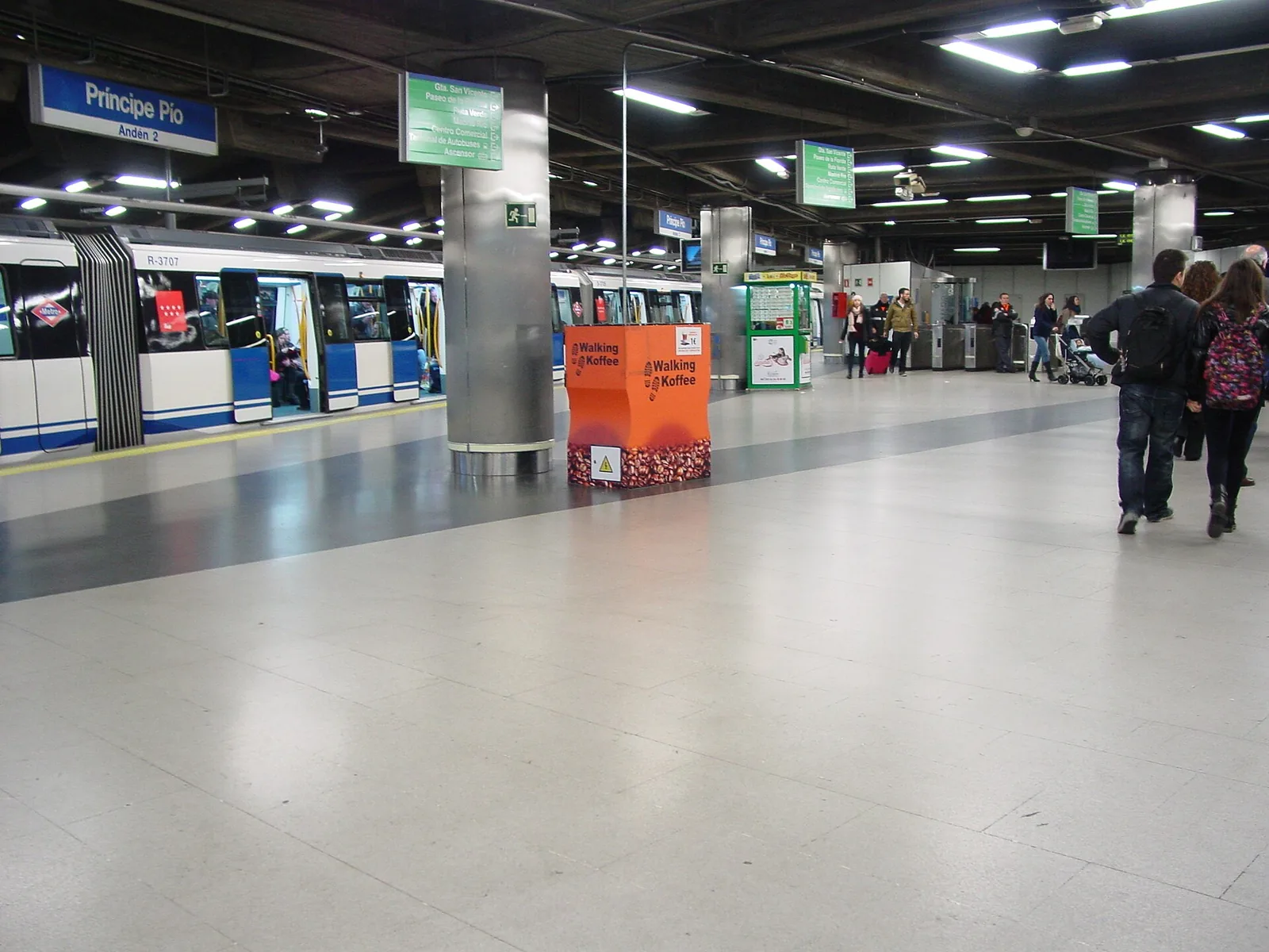A bright metro station platform with a train and passengers in Madrid, Spain