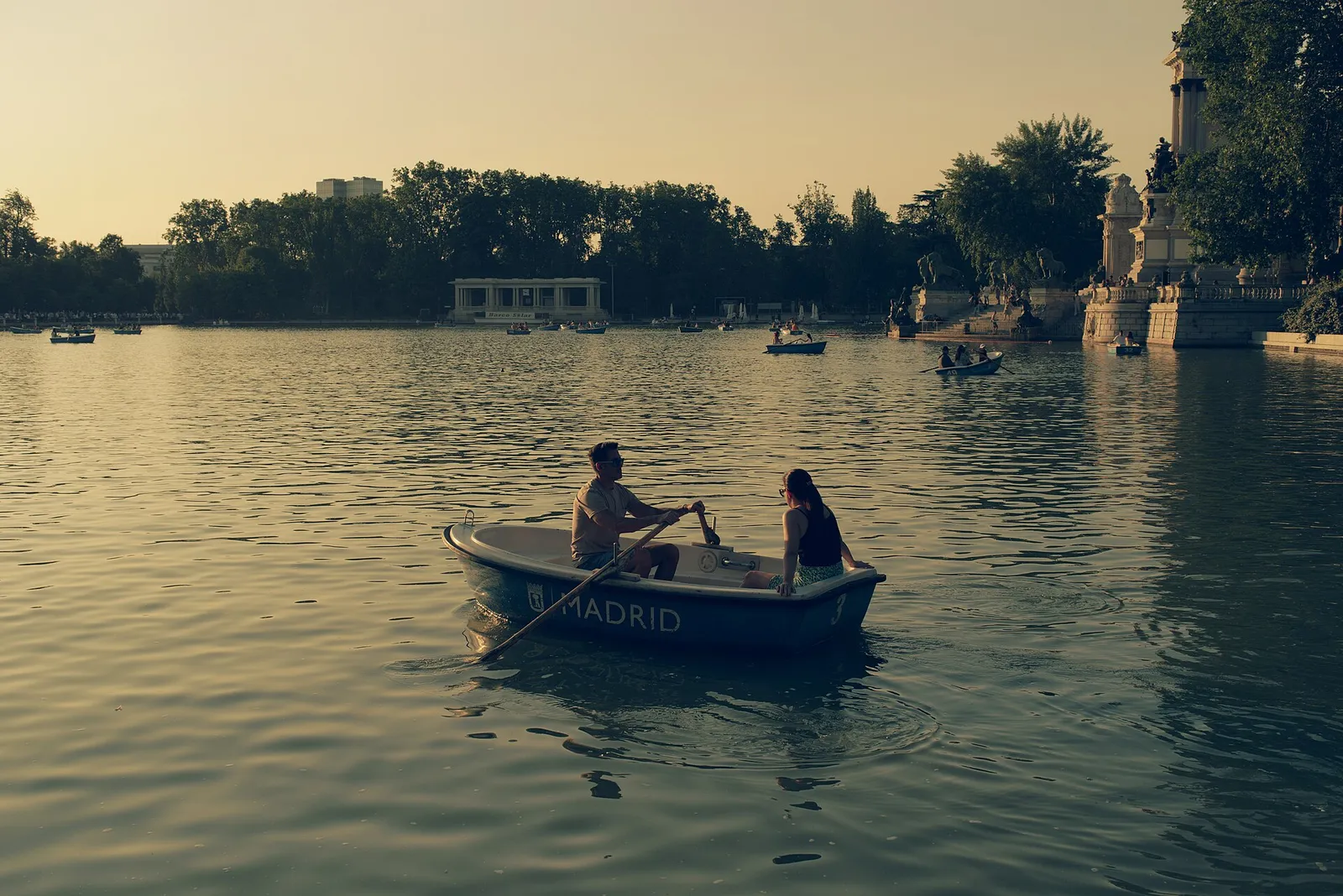 A couple rowing a boat on the Retiro Park lake at golden hour on a summer evening in Madrid