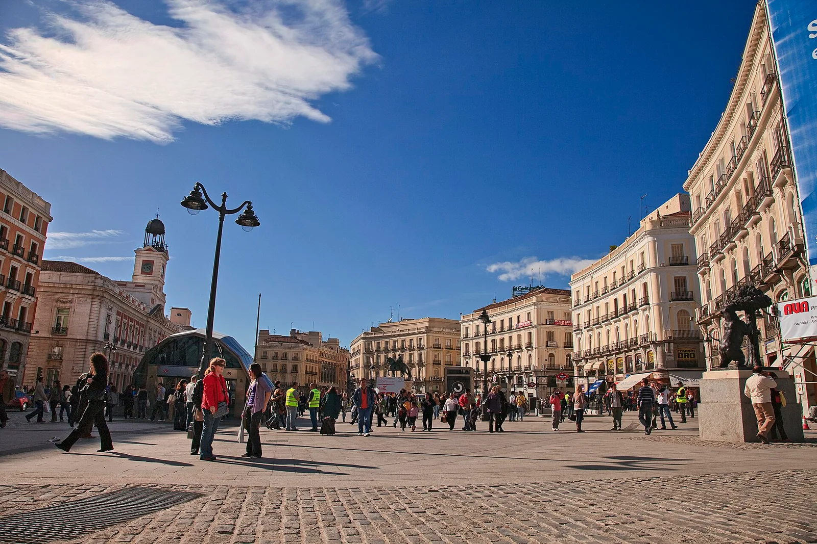 The open square of Puerta del Sol with people walking under a blue sky in Madrid, Spain