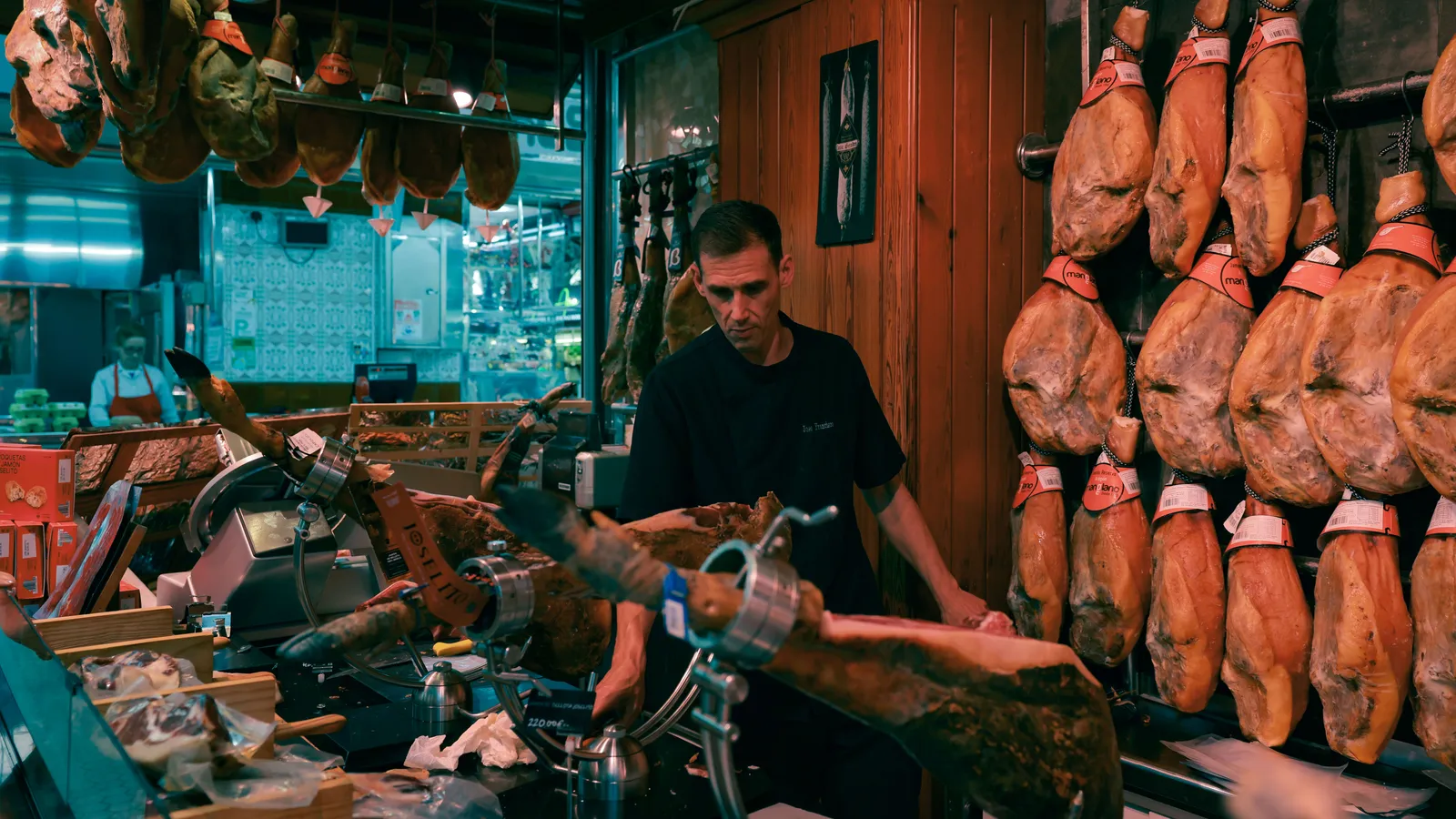A jamon counter in a covered Spanish market hall, whole hams hanging above the slicer