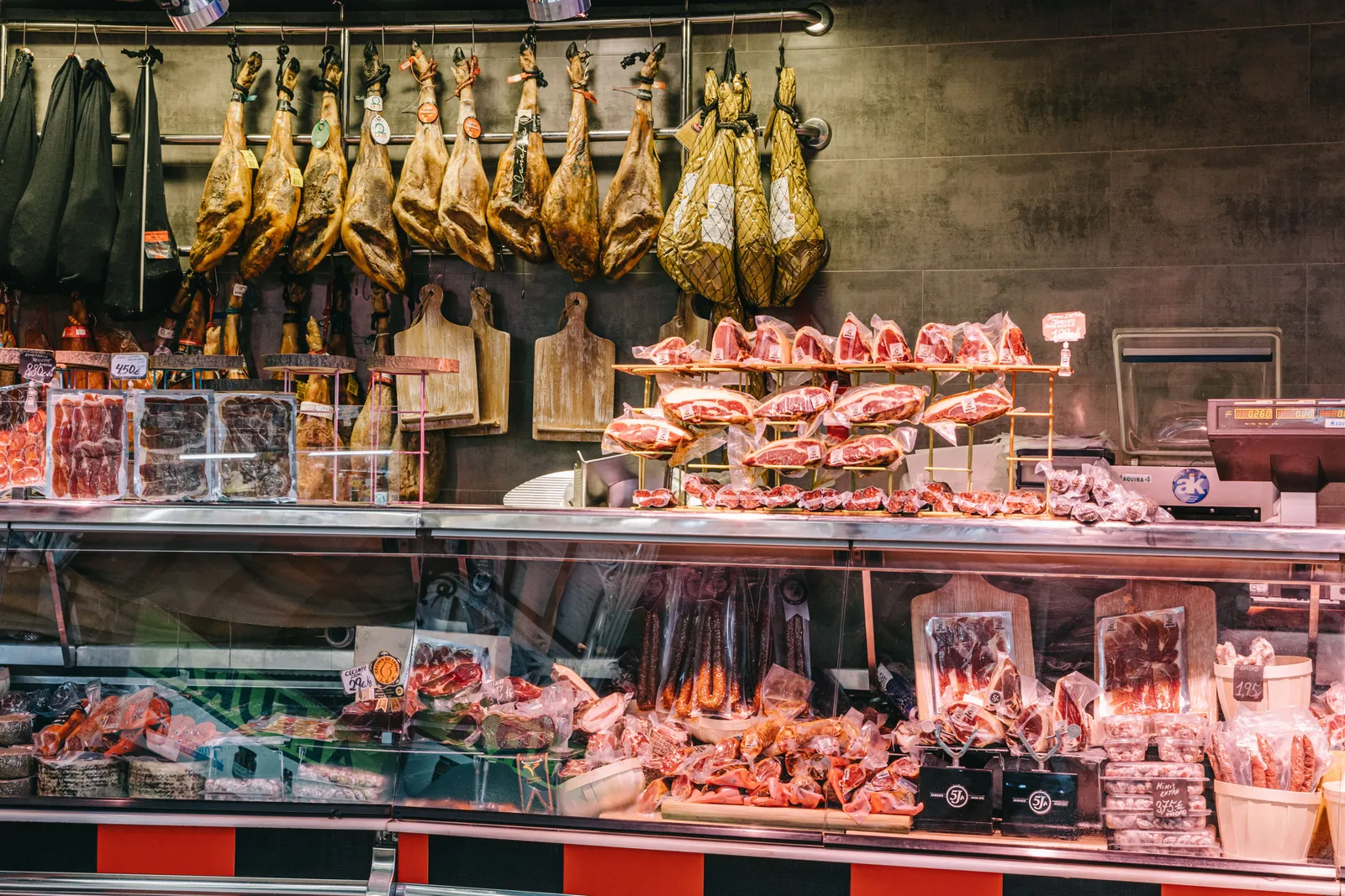 A meat and jamon counter with hanging cured hams inside a covered market in Madrid, Spain