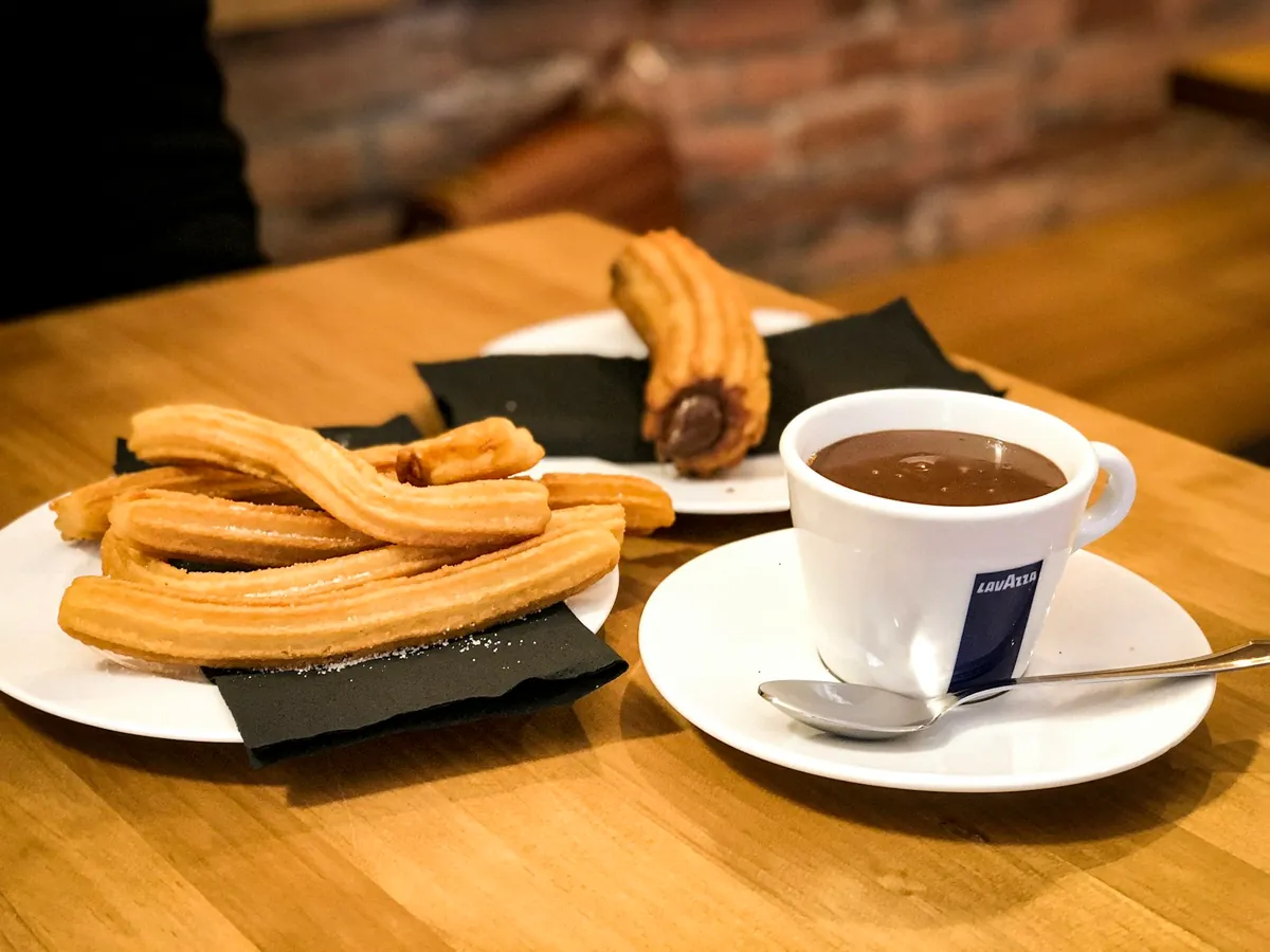 A plate of freshly fried churros served with a cup of thick hot chocolate in Madrid