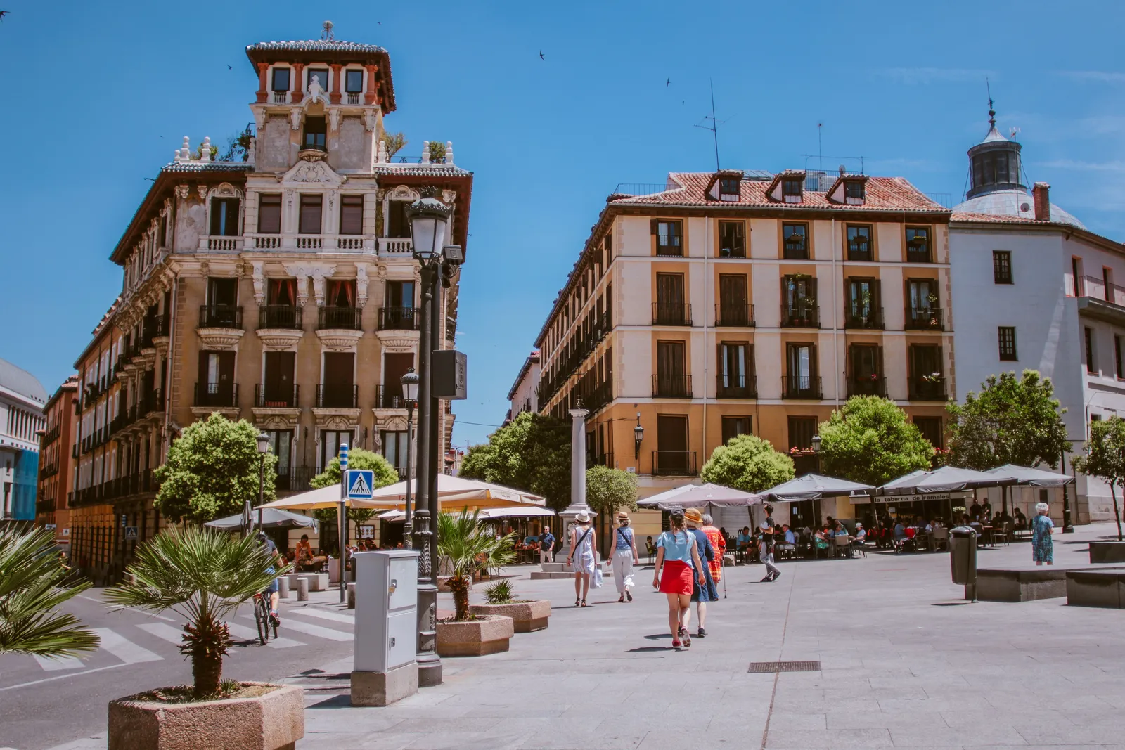 A sunlit square with terrace parasols and pedestrians in central Madrid, Spain