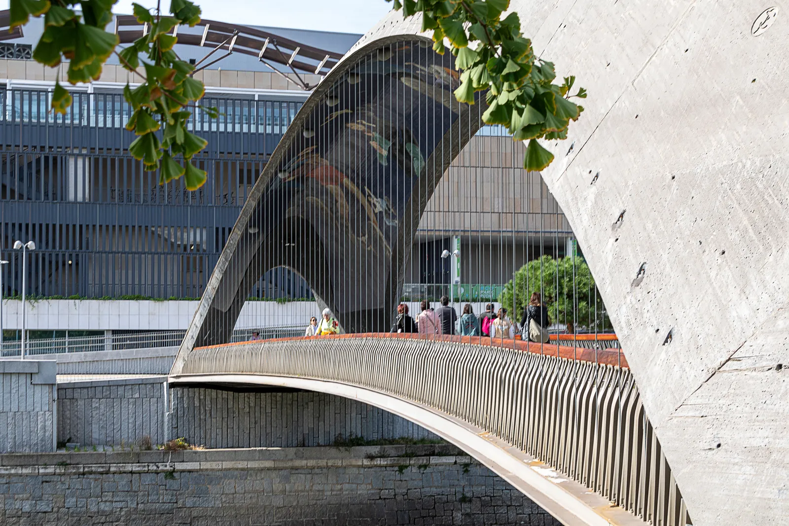 People crossing a modern arched footbridge over the Manzanares river in Madrid Rio park