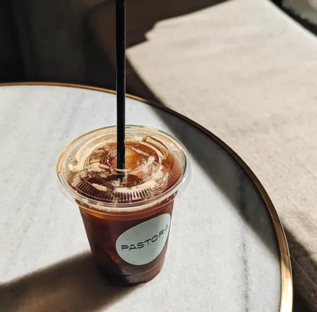 A plastic cup of iced coffee with a black straw on a round marble table