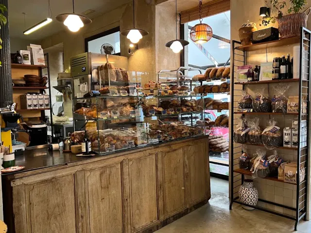 A wooden counter facing a pastry case, loaves of bread on racks and packaged goods