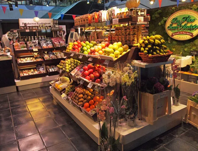 A colourful fruit and vegetable stall in a covered market hall with paper bunting overhead