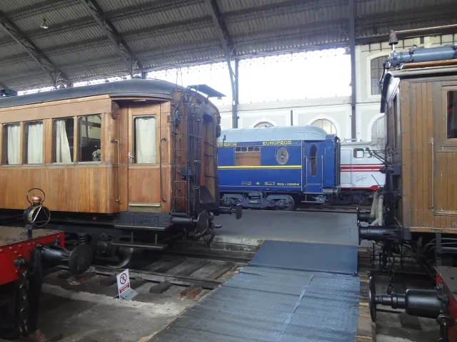 Historic brown and blue railway carriages standing side by side beneath the metal roof of an old platform hall