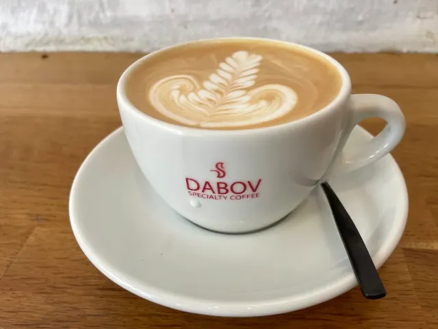 A white cup with a leaf pattern in the foam on a saucer and a wooden table