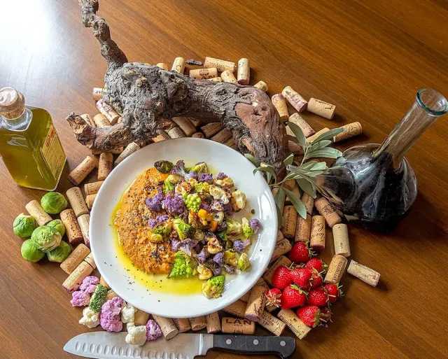 A dish on a white plate with colourful cauliflower in sauce, surrounded by wine corks and a bottle of oil