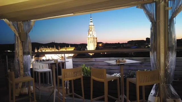 A terrace with high stools facing a lit cathedral tower at dusk
