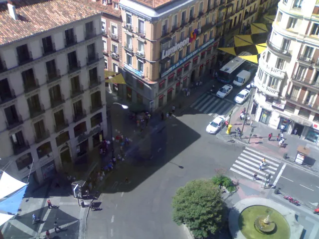 A view from above of a busy city crossroads with pedestrian crossings, taxis and tall stone buildings