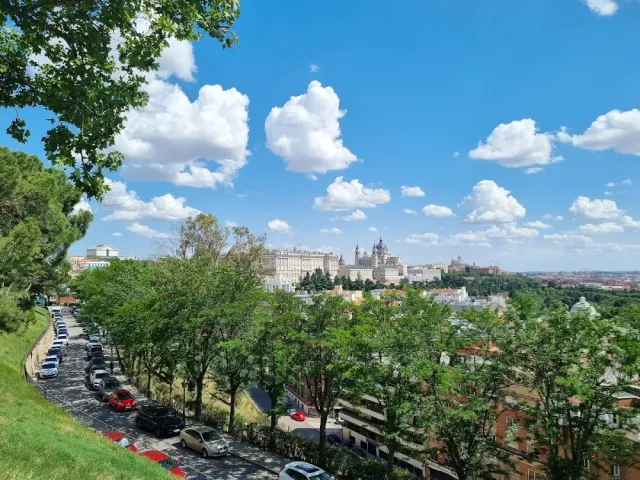 A green slope and trees, and beyond them a large white palace and domes under a blue sky