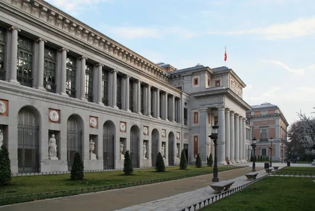 A long neoclassical facade with a row of columns, surrounded by lawn and trees