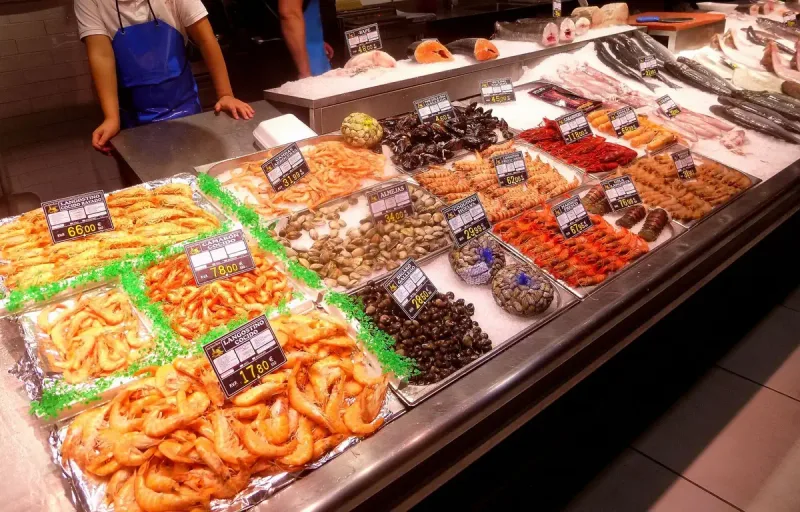 A seafood counter piled with prawns, clams and fish beside price cards at Mercado de la Paz