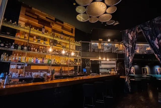 A long lit wooden bar with bottle shelves and round lamps hanging from the ceiling