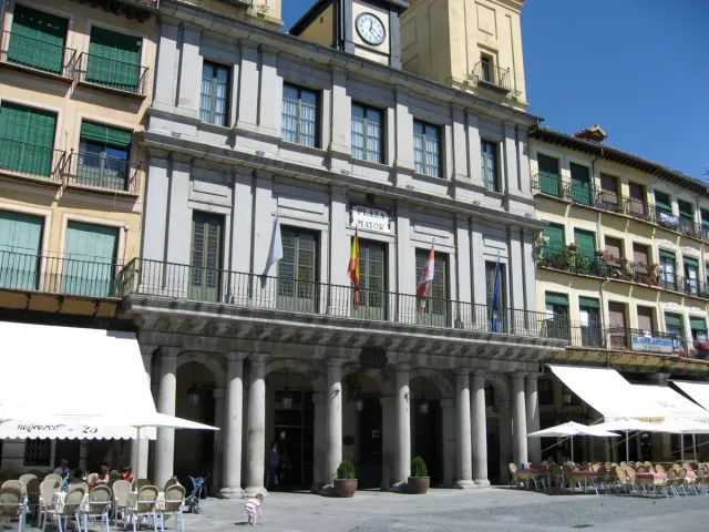 A paved square ringed by arcaded buildings with balconies, awnings and cafe terraces