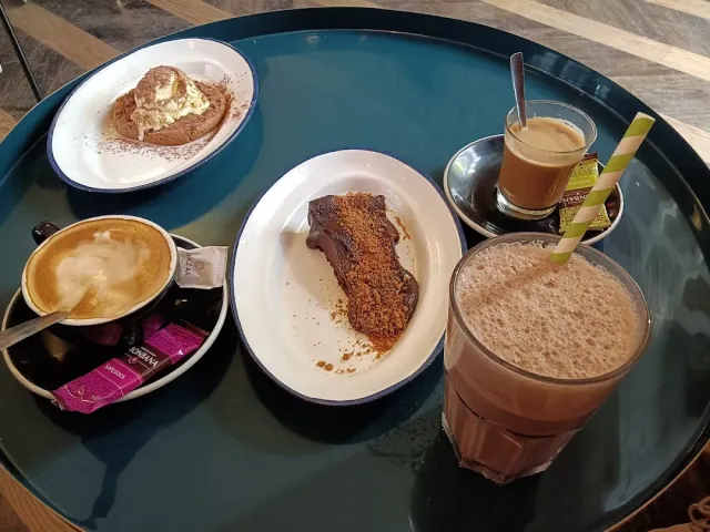 A round tray with a coffee cup, a glass of a brown drink and plates of pastry and cake