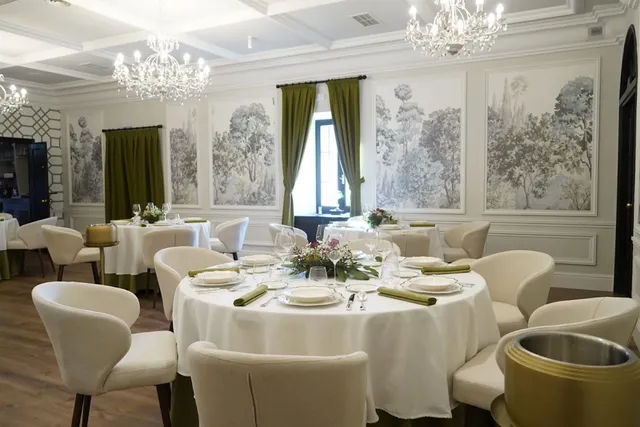 An elegant hall with crystal chandeliers, white chairs and paintings of trees on the walls