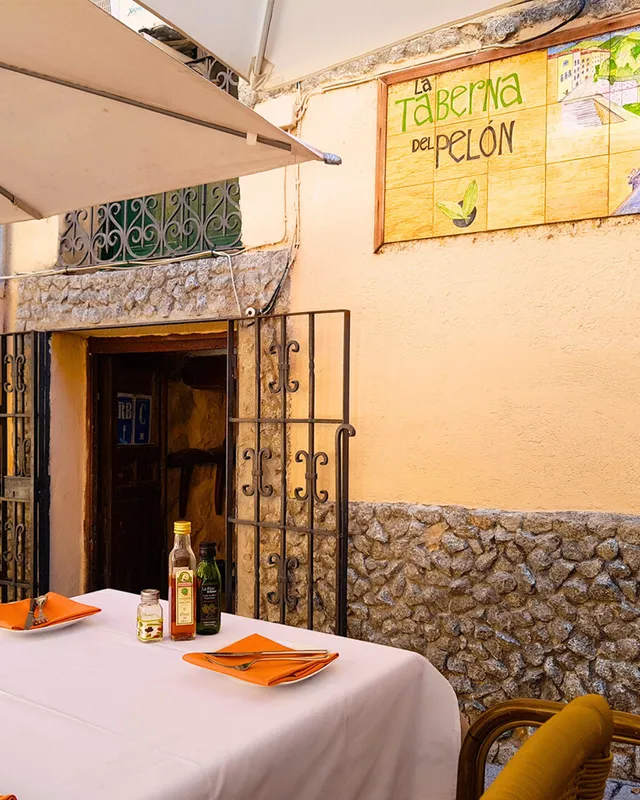 A table set outdoors by a stone wall, a curled iron gate and a painted tile sign