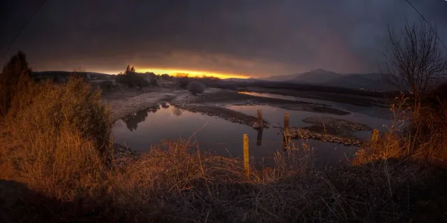 A still reservoir at sunset with an orange sky and mountains reflected in the water
