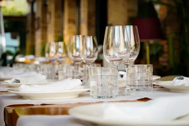 A laid table with wine glasses, ribbed tumblers and white plates with napkins