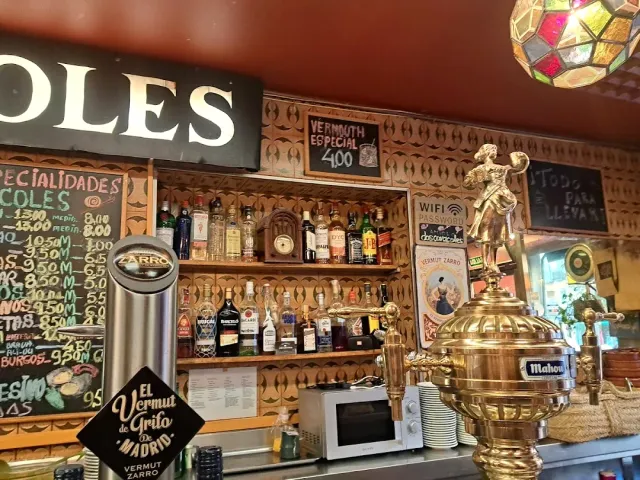 A bar counter with a shiny brass urn, shelves of bottles and chalkboards of the menu