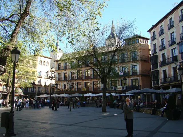 A busy town square with terrace parasols, pedestrians and sand coloured buildings