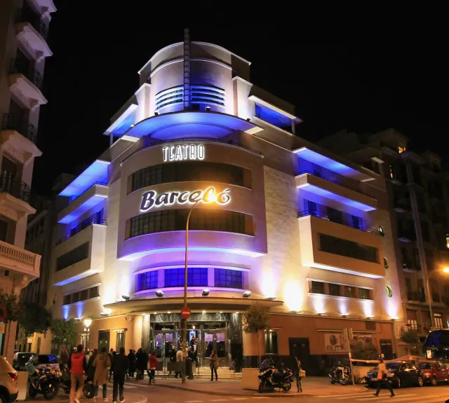 A rounded art deco facade lit in blue and purple at night