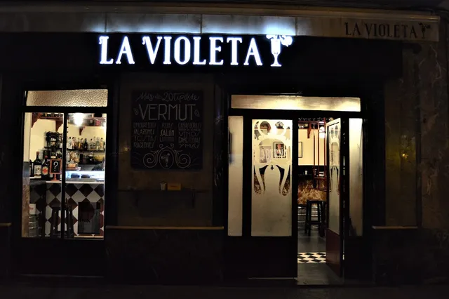 A dark facade at night with a lit sign and a chalkboard behind the window