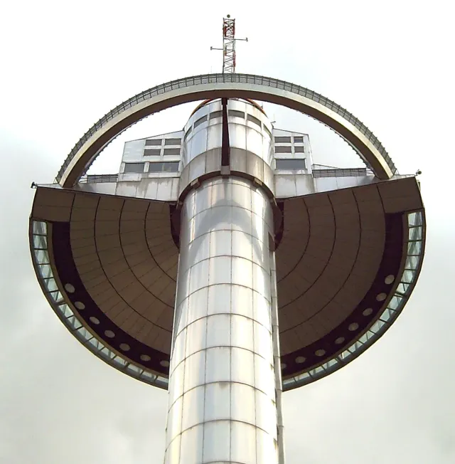 A view from below of a tall concrete tower topped by a circular observation ring against the sky