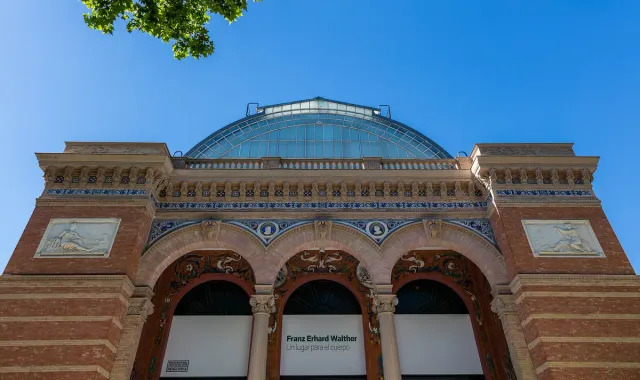 A brick and ceramic tile pavilion with an arched glass roof among park trees