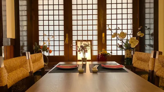 A dining room with latticed paper screens, a long wooden table and red plates set on it