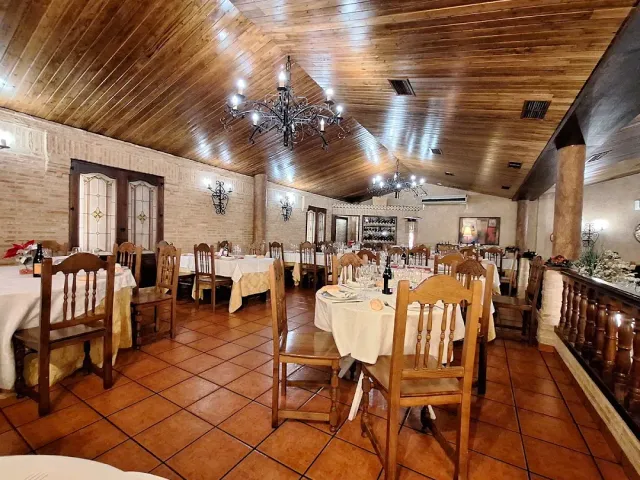 A dining hall with a wooden ceiling, iron chandeliers and tables laid with light cloths