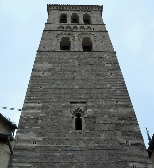 A tall stone and brick bell tower with horseshoe arched windows, photographed from below