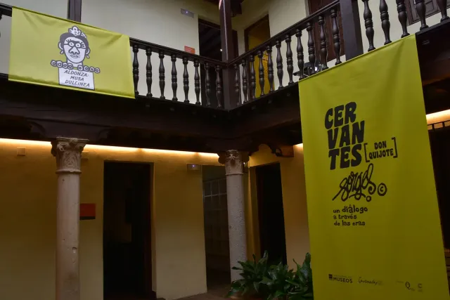 An inner courtyard with a wooden gallery on columns and a hanging fabric banner above the lower floor
