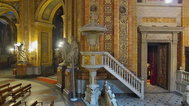 A gilded church interior with a white marble pulpit, a curving staircase and richly decorated columns