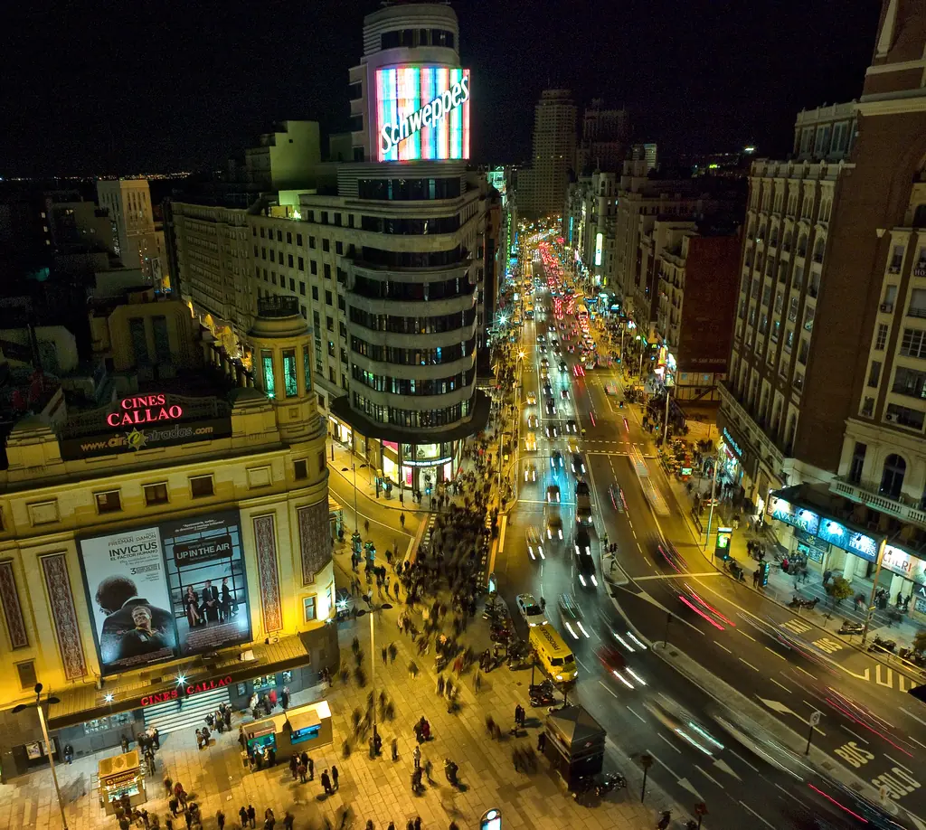 A giant neon sign on the roof of a curved building above a busy avenue at night with car light trails