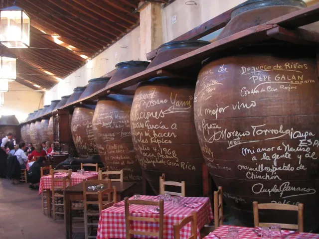 A row of giant clay jars with handwritten inscriptions above tables with checkered cloths