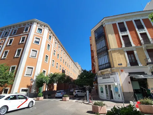 A street corner with orange brick buildings, blue skies and parked cars