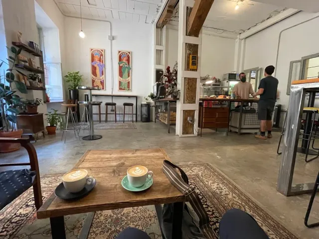Two cappuccino cups on a wooden table in an open space with a rug and a counter