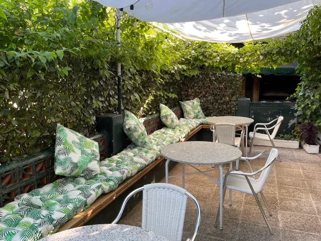 A patio with walls covered in greenery, a bench with printed cushions and round metal tables