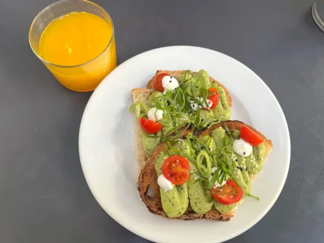 Two slices of bread with avocado spread, cherry tomatoes and a glass of orange juice