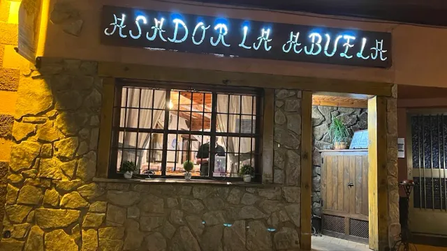 A stone facade at night with a neon sign above a barred window and a wooden door